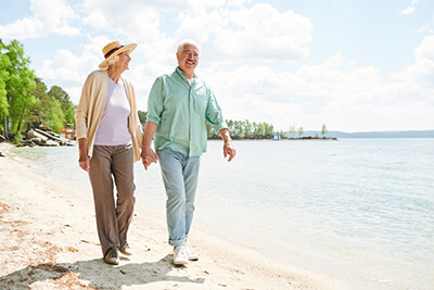 senior couple holding hands walking along the beach for senior living activities