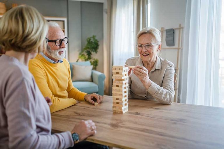 Group of senior people man and woman husband and wife friends or family play leisure board game at home have fun pensioner grandfather and grandmother spend time together with their mature daughter